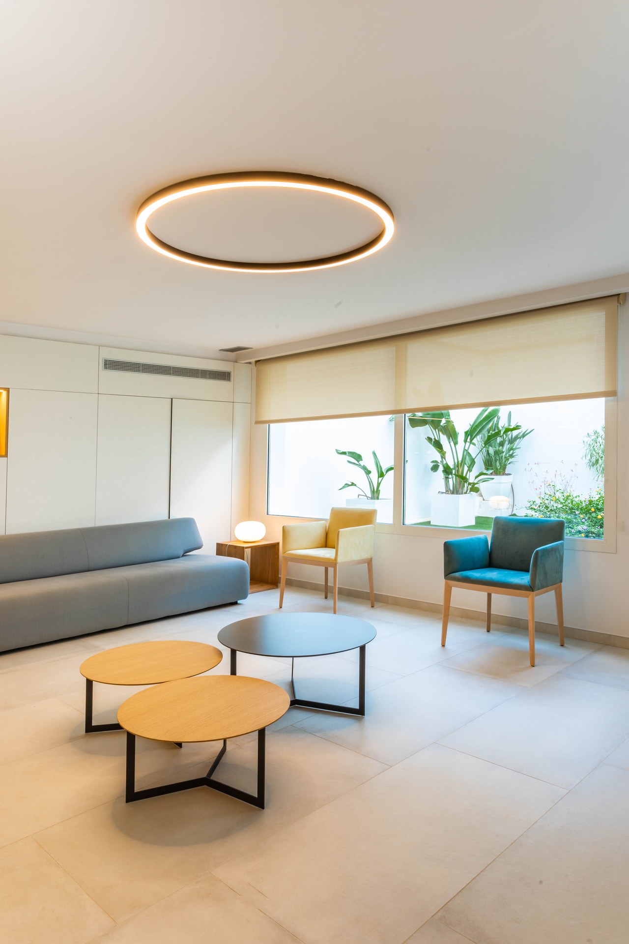 Sala d'espera lluminosa amb sofà gris i taules rodones, Clínica Mir i Andreu